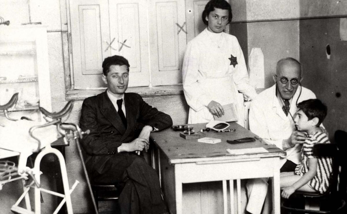 Bedzin, Poland, A doctor examining a child in the ghetto clinic, with a nurse wearing the Jewish badge standing next to him